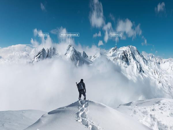 A mountaineer stand on top of a snowy ridge looking at peaks in the distance