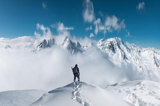 A mountaineer stand on top of a snowy ridge looking at peaks in the distance