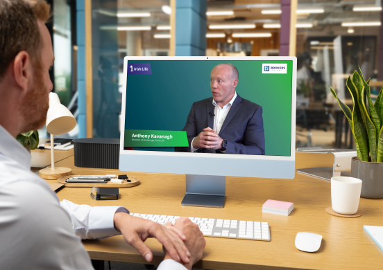 A man sitting at a desk looking at a screen which shows Anthony Kavanagh of Irish Life in conversation